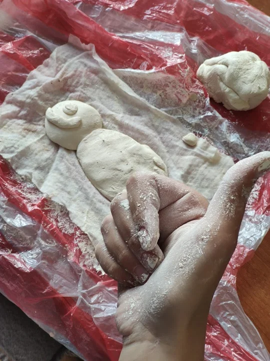 Hands modelling a clay figure at the worktable — from the world of Jasmina and PAGANE